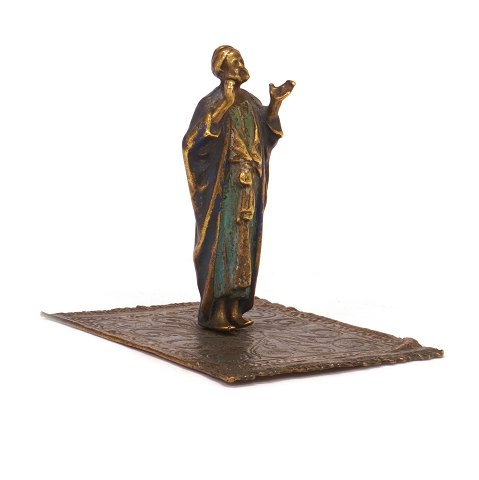 Figur einer orientalischen Person auf einem 
Teppich. Zinn, dekoriert. H: 9,5cm. Base: 9x11cm